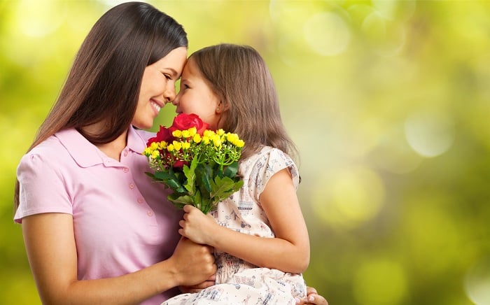 Mother holding her daughter and giving her an Eskimo kiss as they grasp a bouquet of flowers.