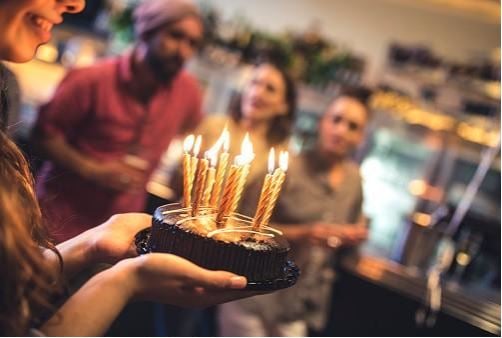 Chocolate birthday cake with candles being carried into a crowd.