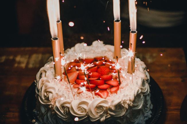 Birthday cake with candles, sparklers, strawberries, and white icing.