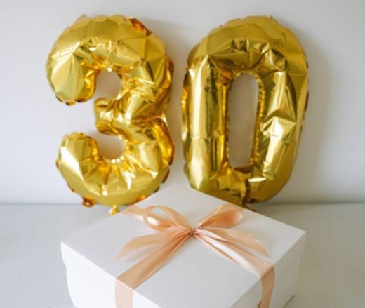 Gold birthday balloons in the shape of the number 30 with a white gift box.