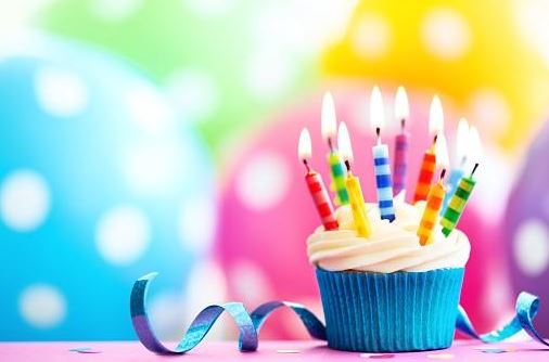 Blue cupcake with birthday candles and balloons in the background