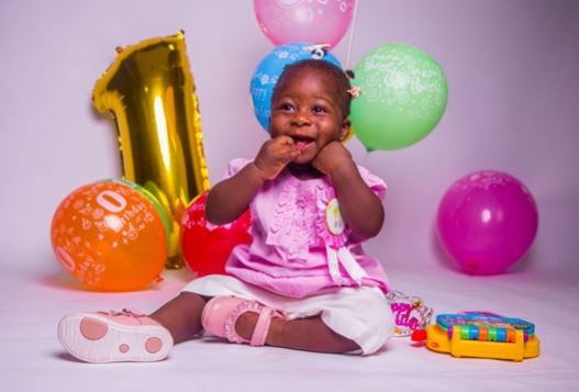 Baby sitting on the floor with a "number one" balloon in the background for her 1st birthday