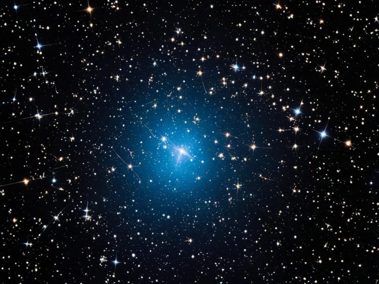 A black night sky is depicted, covered wit many stars and rays of starlight. The bright object in the center is surrounded in blue light and becomes the focal point of the image.