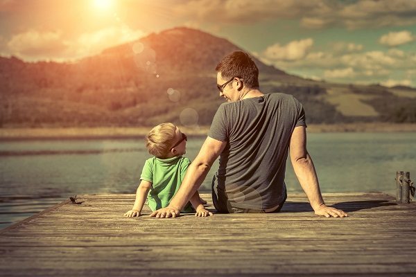 Happiness,Father,And,Son,On,The,Pier,At,Sunny,Day Father and son sitting on a pair looking at each other and smiling