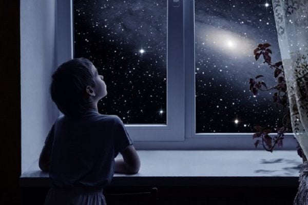 Young boy peering out his window at the stars above