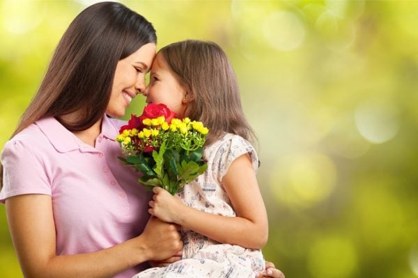 Mother holding her daughter and giving her an Eskimo kiss as they grasp a bouquet of flowers.