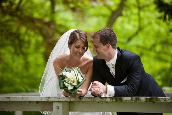 Newly married couple posing for a picture on the edge of a bridge.